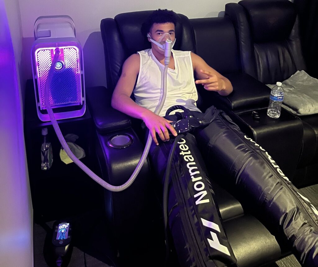 Client relaxing in a recliner during a HEALR hydrogen inhalation session with Normatec recovery boots at LōKAHI Wellness, Kilsyth South